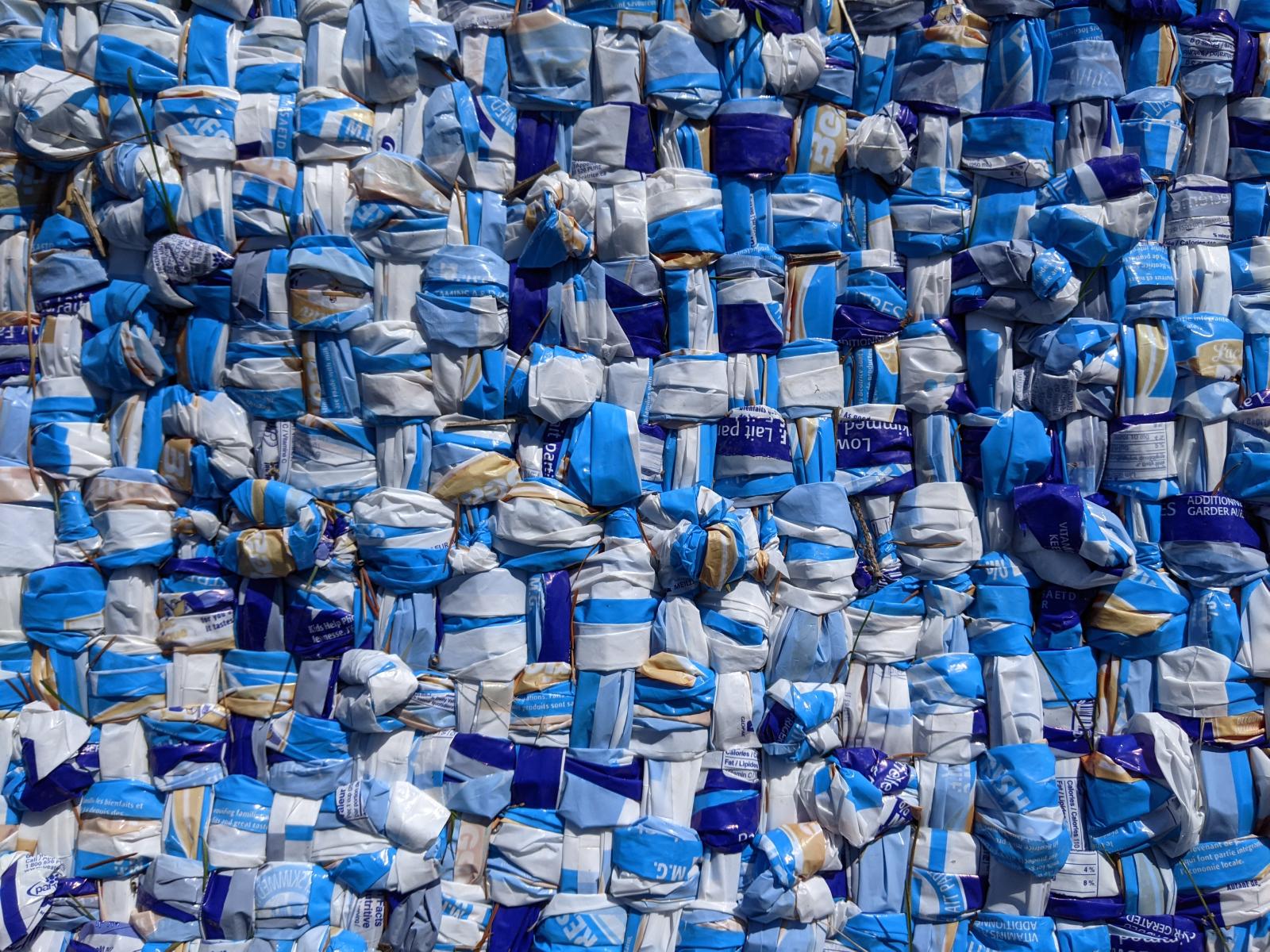 blanket woven from hundreds of milk outer bags: dark blue, light blue, white, yellow. Appears to be from Beatrice 1% 4 litre bags
