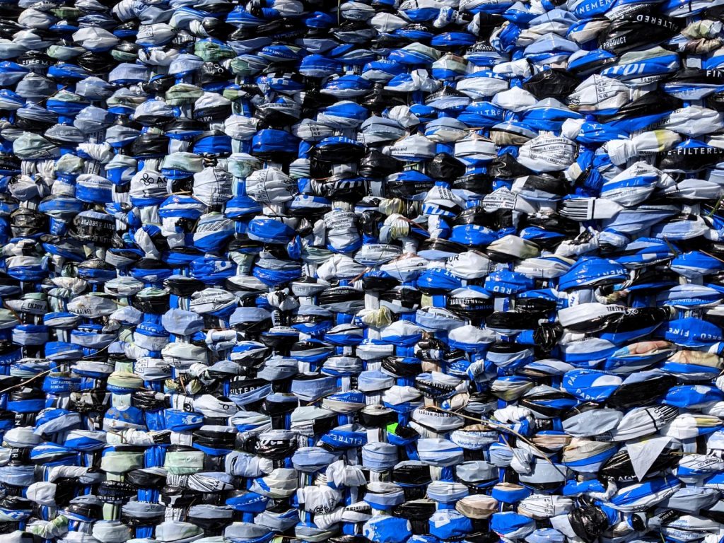 blanket close-up woven from hundreds of milk outer bags: dark blue, light blue, white, black. Snippets of text indicate bags are from Agropur Natrelâ„¢ 2% milk, 4 litres