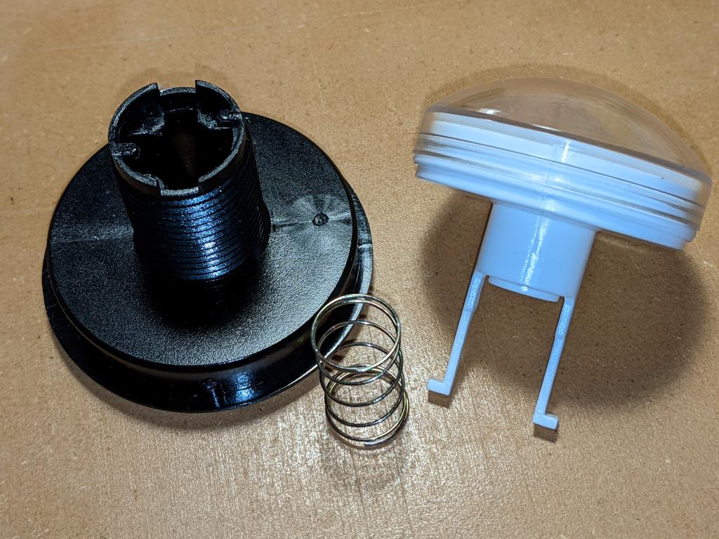 button top components arranged: black threaded button base on left, return spring in the middle, and domed clear top with white underside and white actuators sticking down