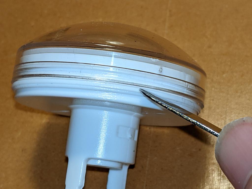 clear button top attached to its white underside. A blunt metal tool (spudger) is pointed at the push-fit join between the two parts