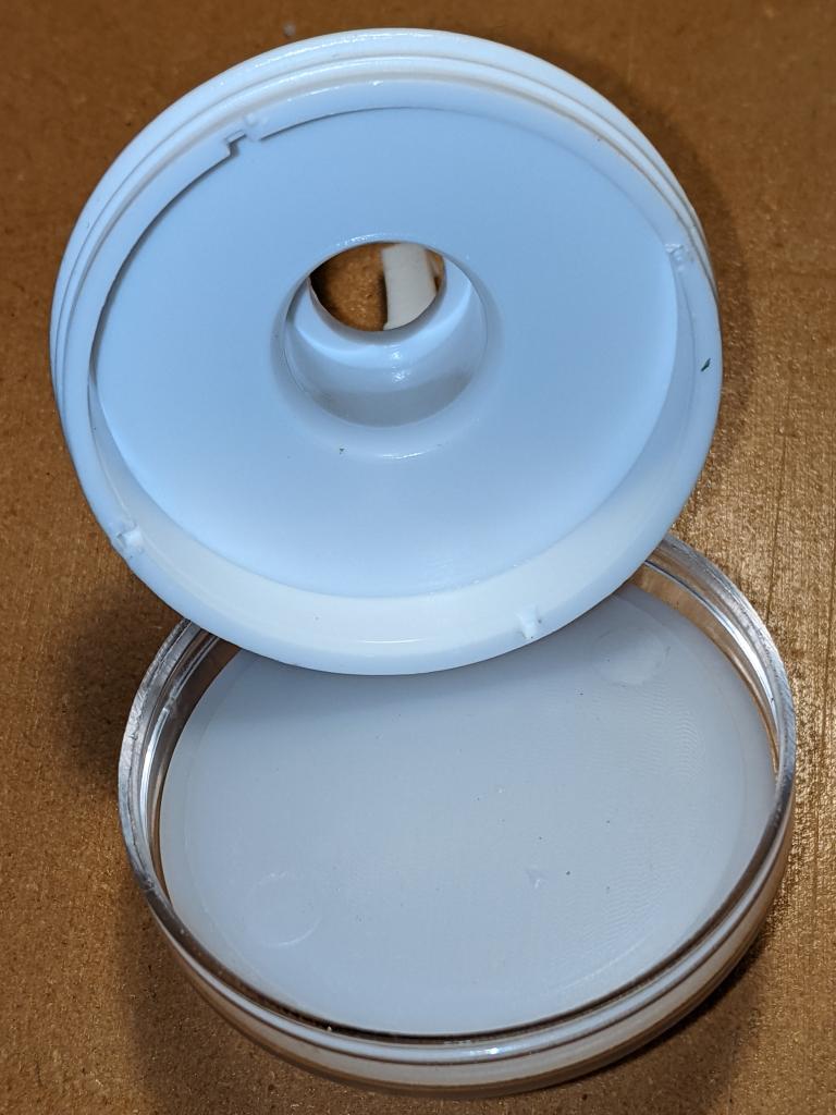 clear button top separated from its white base. A translucent white diffuser is inside the clear top. The white base has a hollow centre and a circular cavity