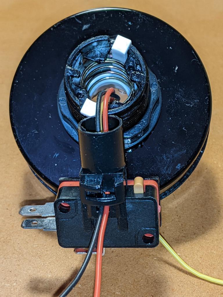 underside of the button shaft, with microswitch attached to LED holder. The wires coming from the LED ring inside the button top have been fed through the small cavities where the original LED holder clips/contacts have been removed. The red/black power wires are on the side towards us, while the yellow data wire is behind the microswitch