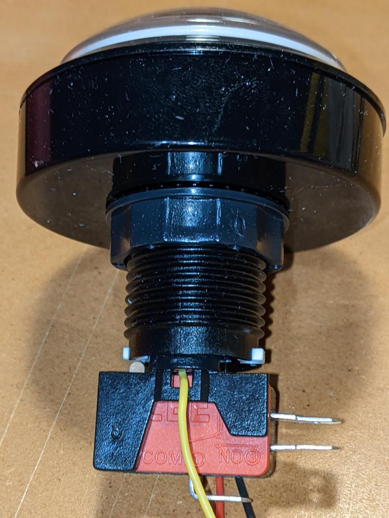 Fully reassembled button, with microswitch installed into its bayonet connector in the threaded shaft, and the button actuator lined up with the microswitch lever on the left. The yellow data wire is in front of the microswitch at bottom