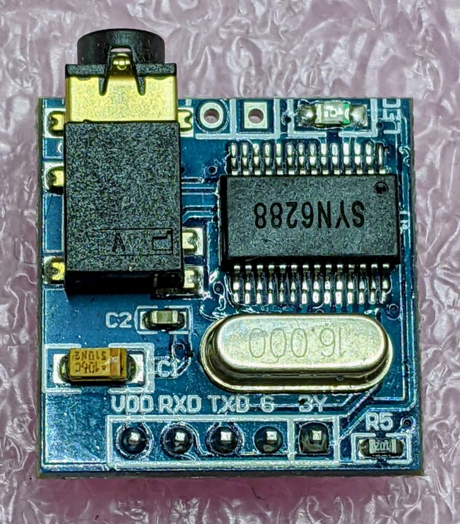 small blue circuit board with 6 MHz crystal oscillator, main chip, input headers at bottom and headphone jack/speaker output at top