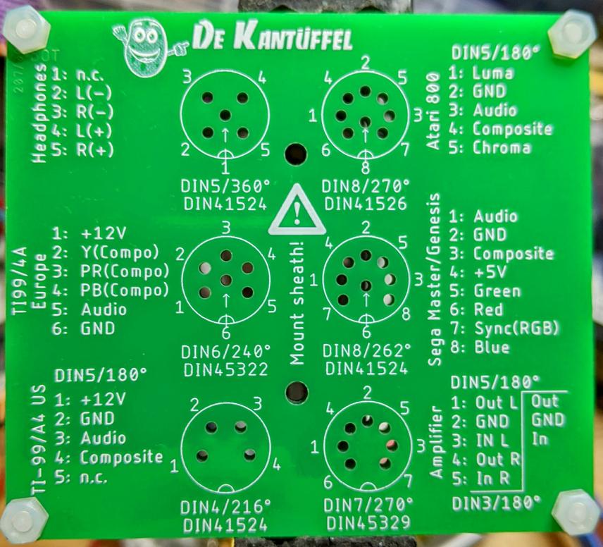 a rectangular green circuit board with markings for various DIN connectors, and holes for the connector pins to fin through. One of the sets of holes is filled by a 7-pin 270° DIN connector, ready for soldering.

There are various pinouts for retrocomputers on the board. There is also the slogan DE KANTÜFFEL, with a smiling cartoon potato next to it